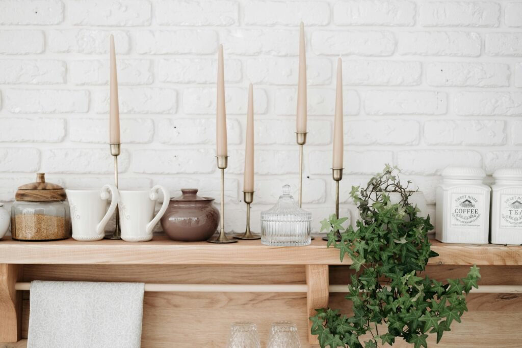 Cozy kitchen shelf with decorative elements like candle holders, mugs, and a potted plant against a white brick wall.